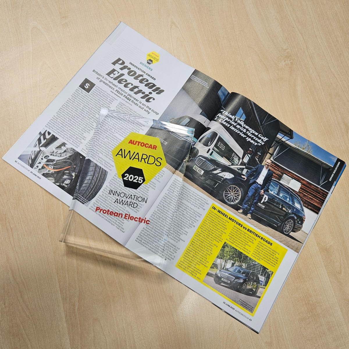 An open magazine with a rectangular glass award laid across the left hand page. Both are on top of a light brown wood surface. The magazine features a news article with pictures.